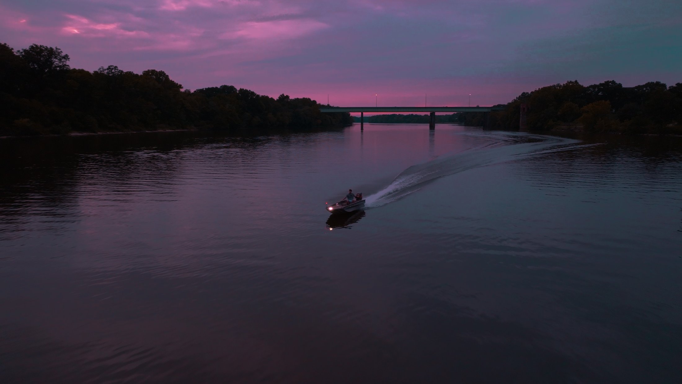 Divine Outdoors Co. boat running down the river at sunset, headed toward the bridge