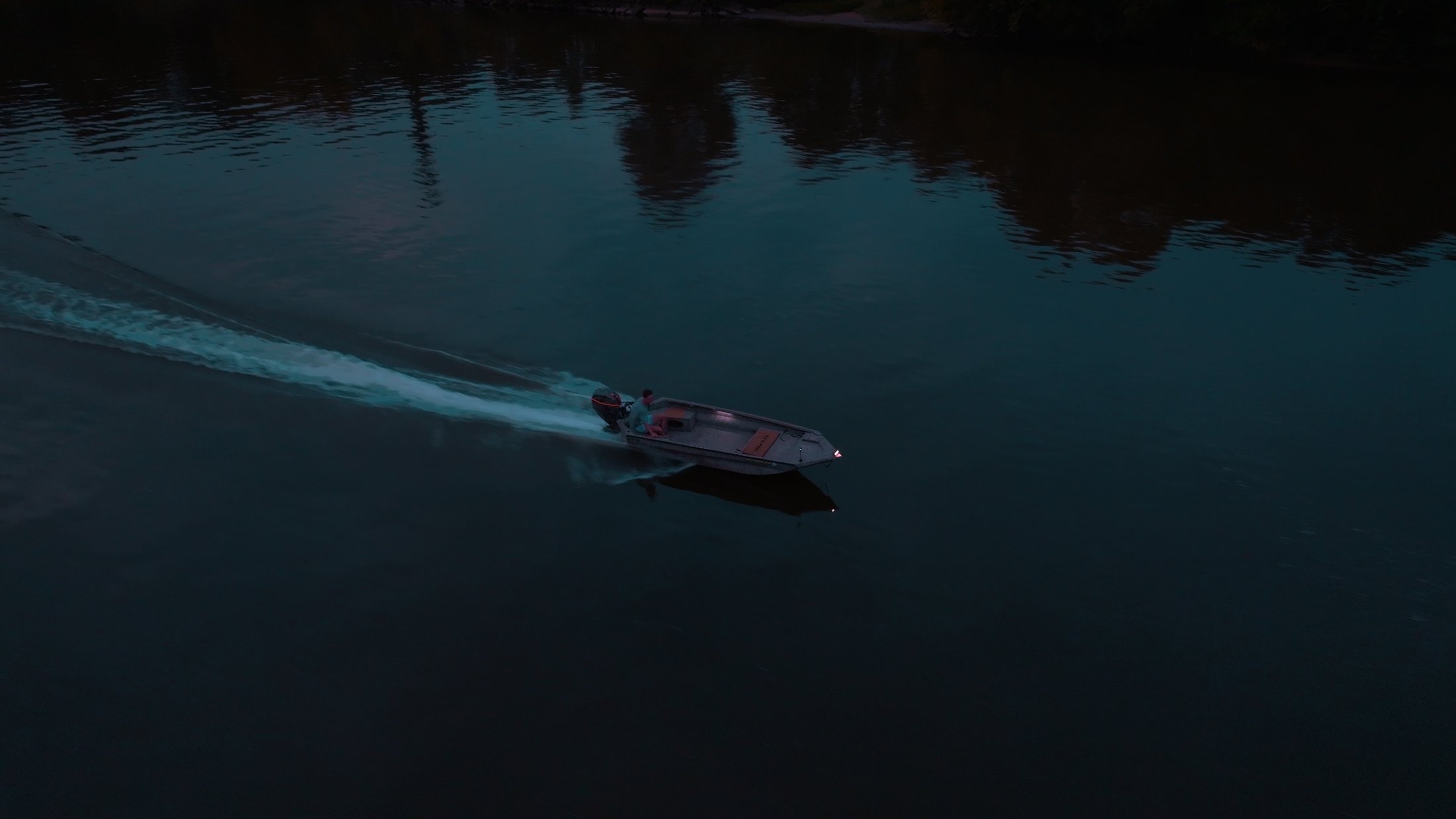 Divine Outdoors Co. boat carving a wake across the river at dusk